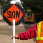 Worker holding a 'SLOW' sign at a construction site.