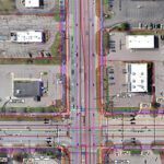 Aerial view of an urban intersection with roads, buildings, and marked utilities.