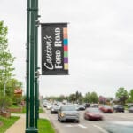 Green tree next to green pole and black flag on street with cars