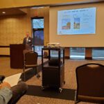 Presenter giving a lecture with slides in a conference room.