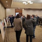 People discuss exhibits at an indoor event in a conference room.