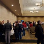 People mingling in a large conference room during a break.