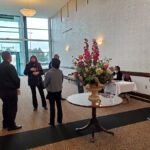 People gathered near a floral arrangement inside a modern building lobby.
