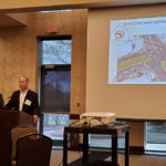 Speaker presenting data on a projector screen in a conference room.