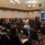 Audience seated in a conference room listening attentively.